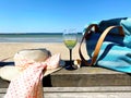 Glass of wine  on restaurant table , women hat with bow beachwear  accessories , seashell  and blue bag , turquoise ocean water  s Royalty Free Stock Photo