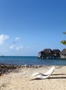 Beach seats on the sandy coast and tropical houses in the distance against the blue sky