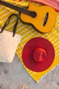 A beach setup features a guitar and a red hat on a yellow blanket Royalty Free Stock Photo