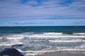 Beach shoreline with foamy waves and boats in distance against a blue sky Royalty Free Stock Photo