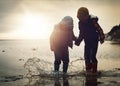 Beach, sunset and silhouette of children in water splash together, holding hands and playing in waves. Fun, holiday and Royalty Free Stock Photo