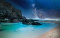 Beach surrounded by the sea and rocks under a bright starry sky at night - perfect for backgrounds Royalty Free Stock Photo