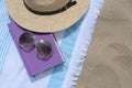 Beach towel with book, sunglasses and straw hat on sand, flat lay. Space for text Royalty Free Stock Photo