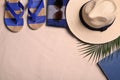 Beach towel, hat, sunglasses, book, tropical leaf and flip flops on sand, flat lay. Space for text