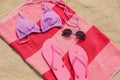 Beach towel with slippers, sunglasses and swimsuit on sand, top view Royalty Free Stock Photo