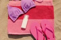 Beach towel with slippers, sunscreen and swimsuit on sand, flat lay Royalty Free Stock Photo