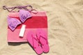 Beach towel with slippers, sunscreen and swimsuit on sand, flat lay. Space for text Royalty Free Stock Photo