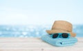 Beach towel, sunglasses and hat on wood over blurred seascape