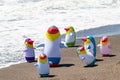 Beach toy background. Selective focus on a group of seven colorful inflatable rubber penguin toys at a sandy sunny beach. Space