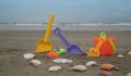 Beach toys, shovels and bucket on the sand surrounded by shells with the sea and blue sky in the background Royalty Free Stock Photo