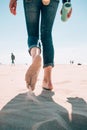 Beach travel - woman in a jeanse walking on sand beach leaving footprints in the sand. Closeup detail of female feet and Royalty Free Stock Photo