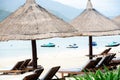 Beach umbrella thatched with palm leaves, lounge chairs, white sandy shoreline and row of personal watercraft blurry background, Royalty Free Stock Photo