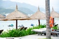 Beach umbrella thatched with palm leaves, lounge chairs, white sandy shoreline and row of personal watercraft blurry background, Royalty Free Stock Photo