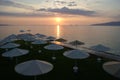 Beach umbrellas, view of the sun setting in the Aegean sea, on the orange sky background, Kalamaki Beach, Isthmia, Greece