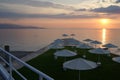 Beach umbrellas, view of the sun setting in the Aegean sea, on the orange sky background, Kalamaki Beach, Isthmia, Greece