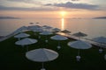 Beach umbrellas, view of the sun setting in the Aegean sea, on the orange sky background, Kalamaki Beach, Isthmia, Greece