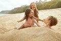 Beach Vacation. Family Enjoying Summertime At Tropical Resort. Little Sister Feeds Her Buried In Sand Brother Fruit. Royalty Free Stock Photo