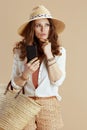 pensive trendy female in blouse and shorts using phone on beige