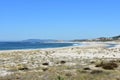 Beach with vegetation in sand dunes and lighthouse. Blue sea with waves and foam, sunny day. Galicia, Spain. Royalty Free Stock Photo