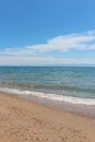 Beach with wave and wet sand with pebble on blue sky and mountains. Sea, ocean background. Vacation outdoor and travel holiday Royalty Free Stock Photo