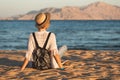 Beach woman happy in hat having summer fun during travel holidays vacation. Girl sits on the sand and looks at the water Royalty Free Stock Photo