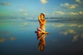 Beach yoga. Attractive woman practicing Gomukhasana Garudasana. Cow Face Pose with Eagle Arms. Water reflection. Slim fit body.