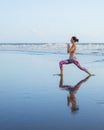 Beach yoga. Slim Caucasian woman practicing Virabhadrasana II, Warrior II Pose. Strong body. Healthy lifestyle. Water reflection. Royalty Free Stock Photo