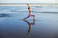 Beach yoga. Slim Caucasian woman practicing Virabhadrasana II, Warrior II Pose. Strong body. Healthy lifestyle. Water reflection. Royalty Free Stock Photo