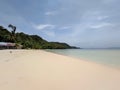 beachfront view on an island with white sand, clear blue sea water and small hills overgrown with green trees.