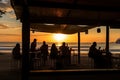 beachside eatery, with view of sunset over the ocean, and silhouettes of people on the sand