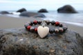 a beaded bracelet with a heart charm on a pebbled beach stone