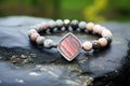 beaded bracelet with a silver charm resting on a marbled stone