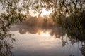 Beautiful landscape of the mirror on the lake during sunrise framed with tree. Light fog over the water. Specular reflection in