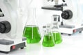 beaker of green chemical on table with blurred microscope Royalty Free Stock Photo