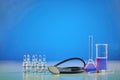 Beaker, medical flask. Purple chemical reagent. Six ampoules with liquid, syringe and phonendoscope, blue background