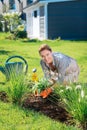 Beaming blonde-haired family woman watering her flowers bed outside