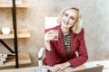 Beaming blonde woman in red jacket wearing bulky gold jewelry