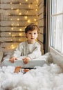 Beaming curlyhair boy opening his christmas gift. New Year lights background