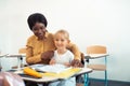 Beaming helpful teacher hugging cute blue-eyed smart girl