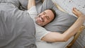 Beaming middle-aged man with grey hair joyfully stretching arms waking up in his cozy bedroom bed, relishing the comfort of a Royalty Free Stock Photo