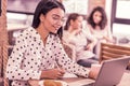 Beaming woman wearing spotted blouse looking at her laptop reading message