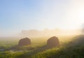 Beams of early morning sunlight shine on two bales of hay in a foggy agricultural field Royalty Free Stock Photo