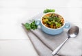 Bean soup in a ceramic blue bowl with tomatoes, olives and parsley, a spoon on a white wooden background Royalty Free Stock Photo