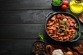 Beans with sausages in tomato sauce on a black plate. Top view. Royalty Free Stock Photo