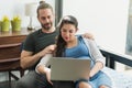 Beard man and his pregnant wife watching movie on laptop feeling happy while sitting on sofa in the home. Family concept Royalty Free Stock Photo