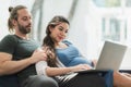 Beard man and his pregnant wife watching movie on laptop feeling happy while sitting on sofa in the home. Family concept Royalty Free Stock Photo