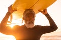 Bearded african american senior man carrying surfboard on head at beach against clear sky at sunset Royalty Free Stock Photo