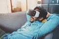 Bearded african man enjoying virtual reality glasses while relaxing on sofa at home.Blurred background,flare. Royalty Free Stock Photo