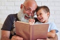 Bearded aged man and his grandson having fun reading a book toge Royalty Free Stock Photo