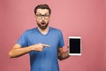 Bearded amazed man in eyeglasses which showing blank tablet computer screen and looking at camera. Isolated over pink background Royalty Free Stock Photo